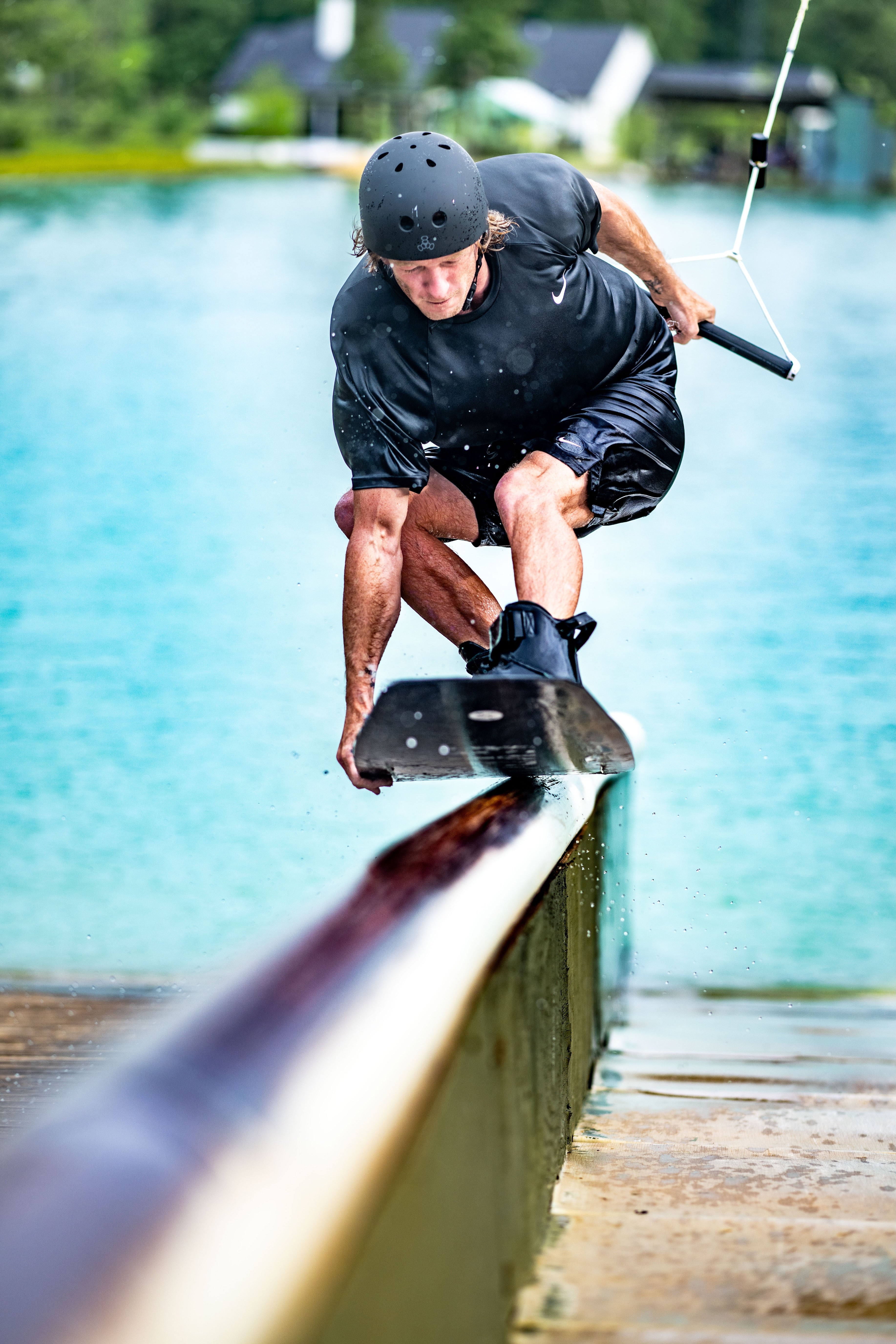 Person wakeboarding on a rail with a helmet and calm water in the background.