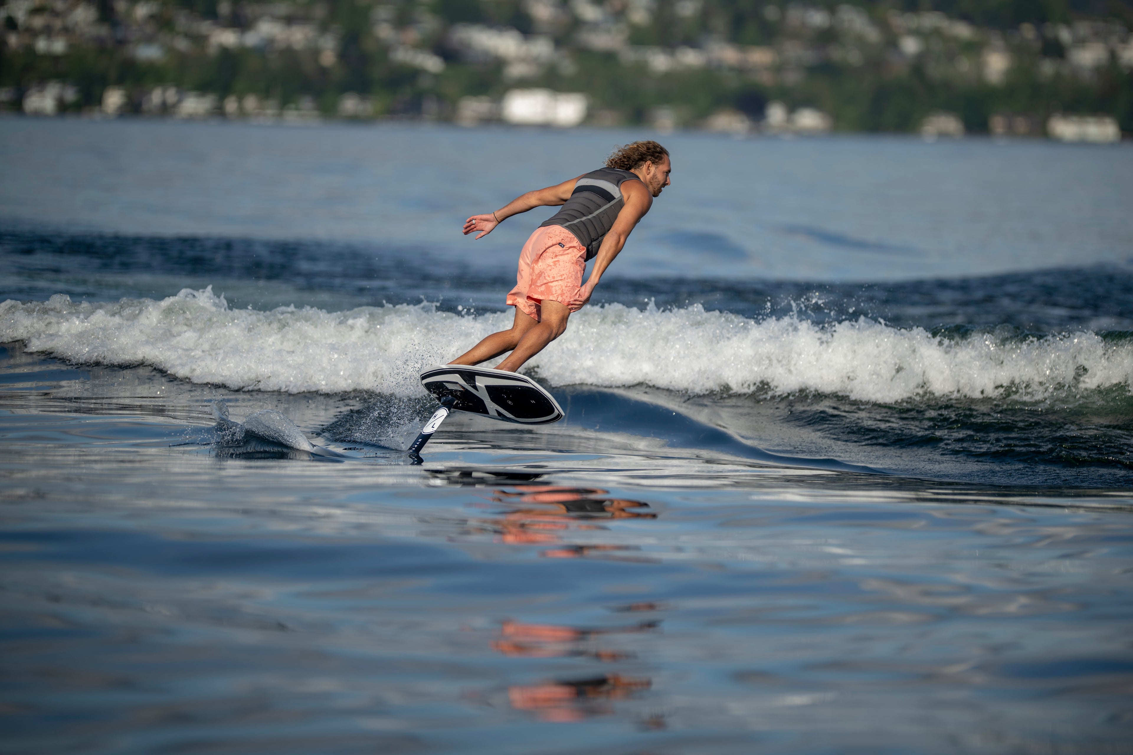 Person hydrofoiling on a lake with a cityscape and trees in the background.