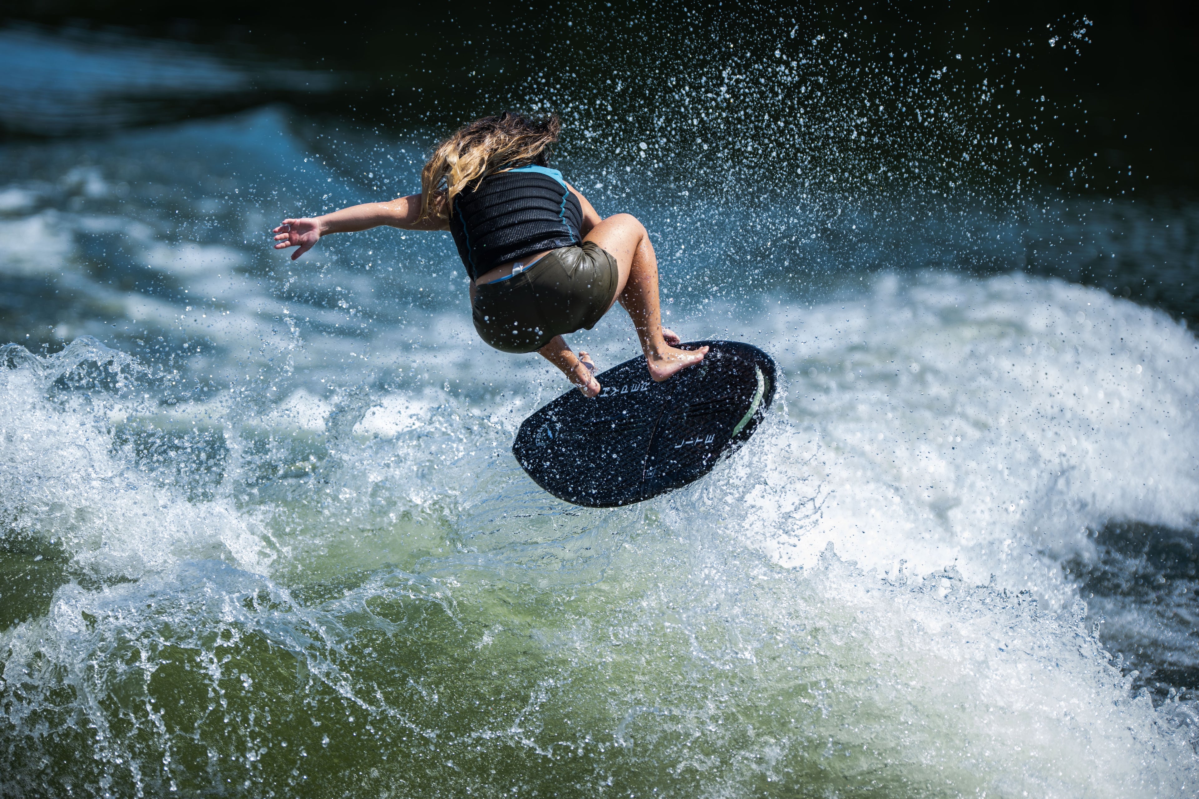 Person surfing a wave, airborne with spray and a dark wet suit.