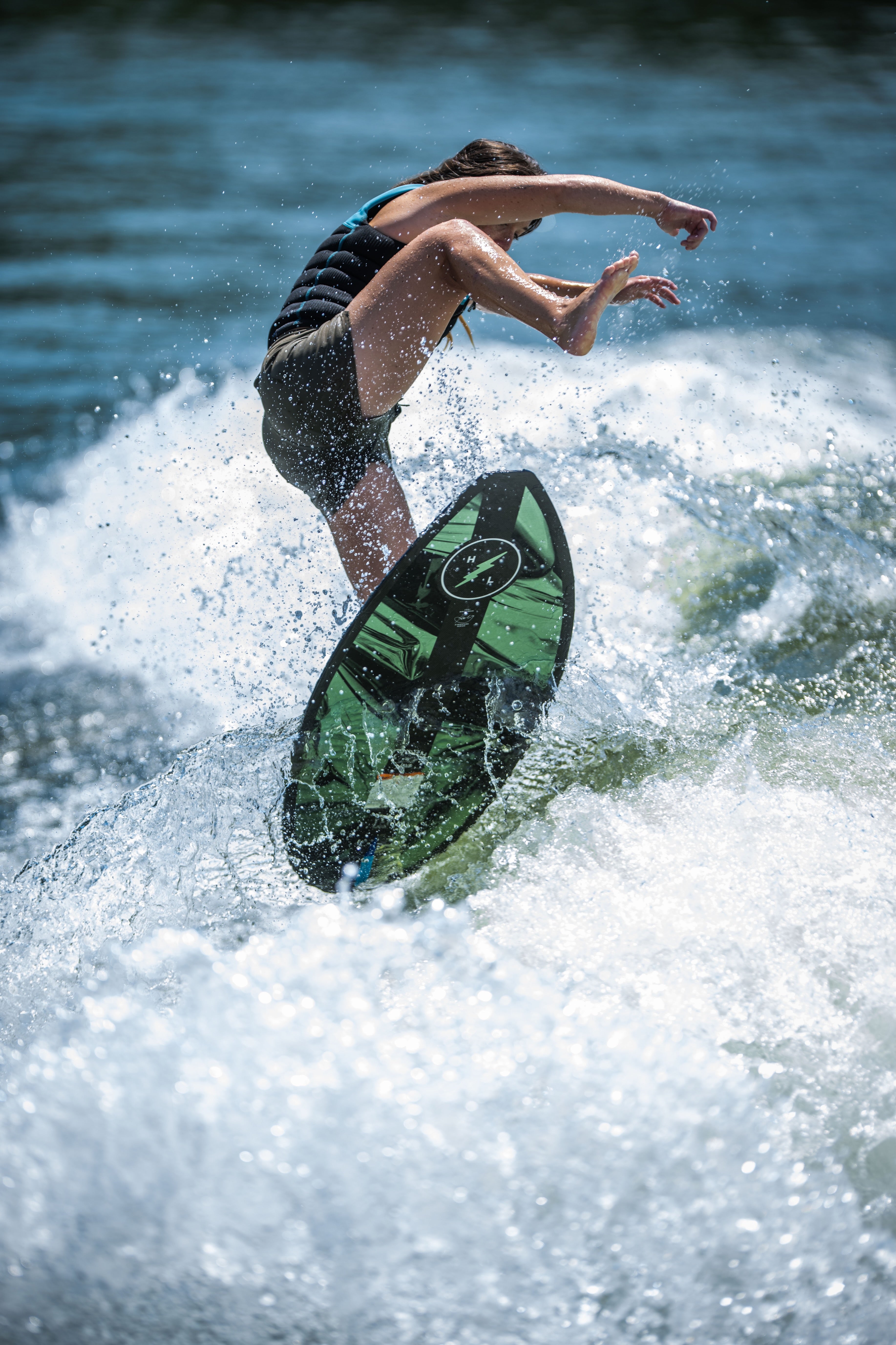 Person surfing on green board, mid-air, surrounded by splashing waves.