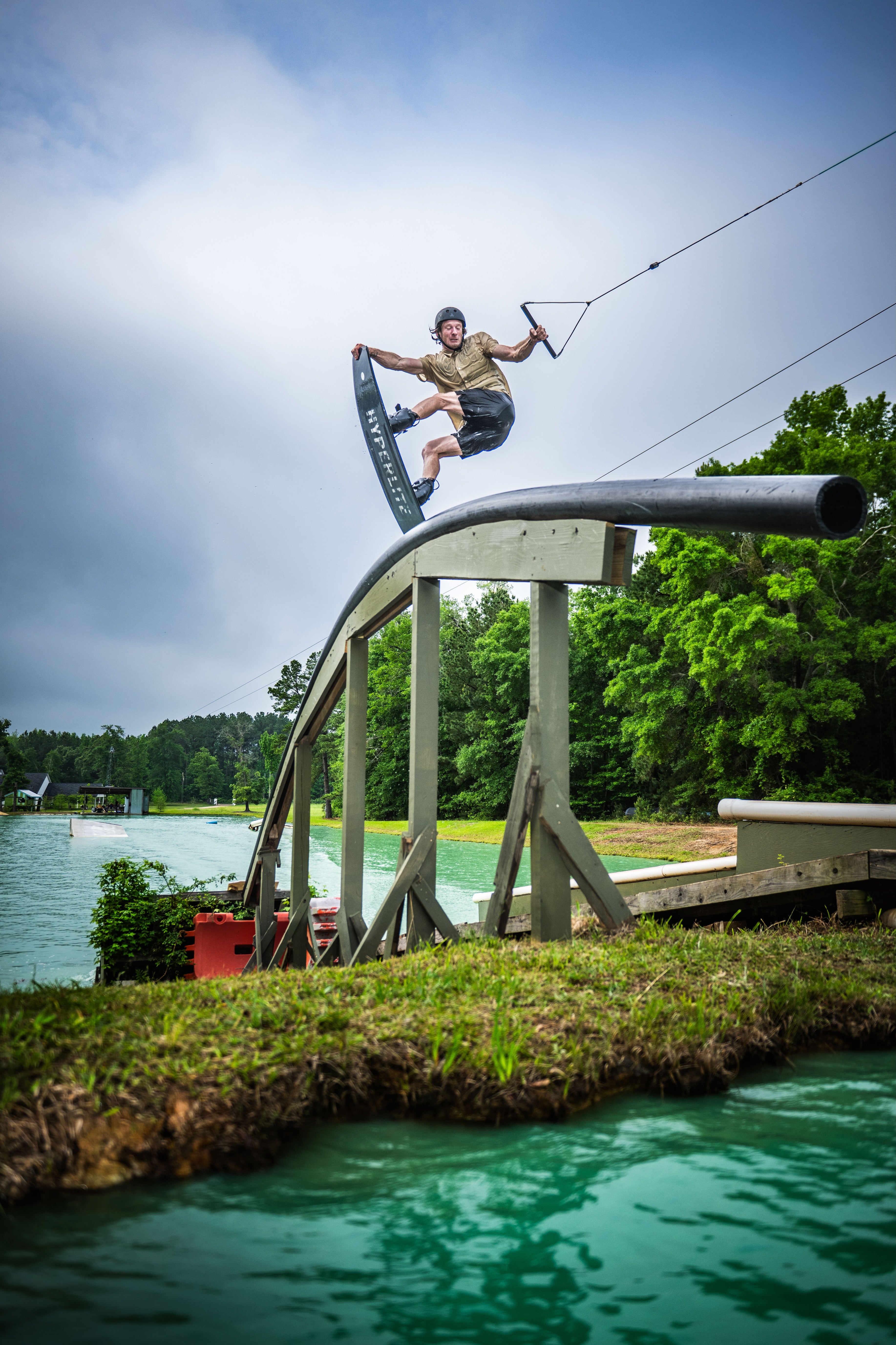 Person wakeboarding on a rail above water, surrounded by green foliage.