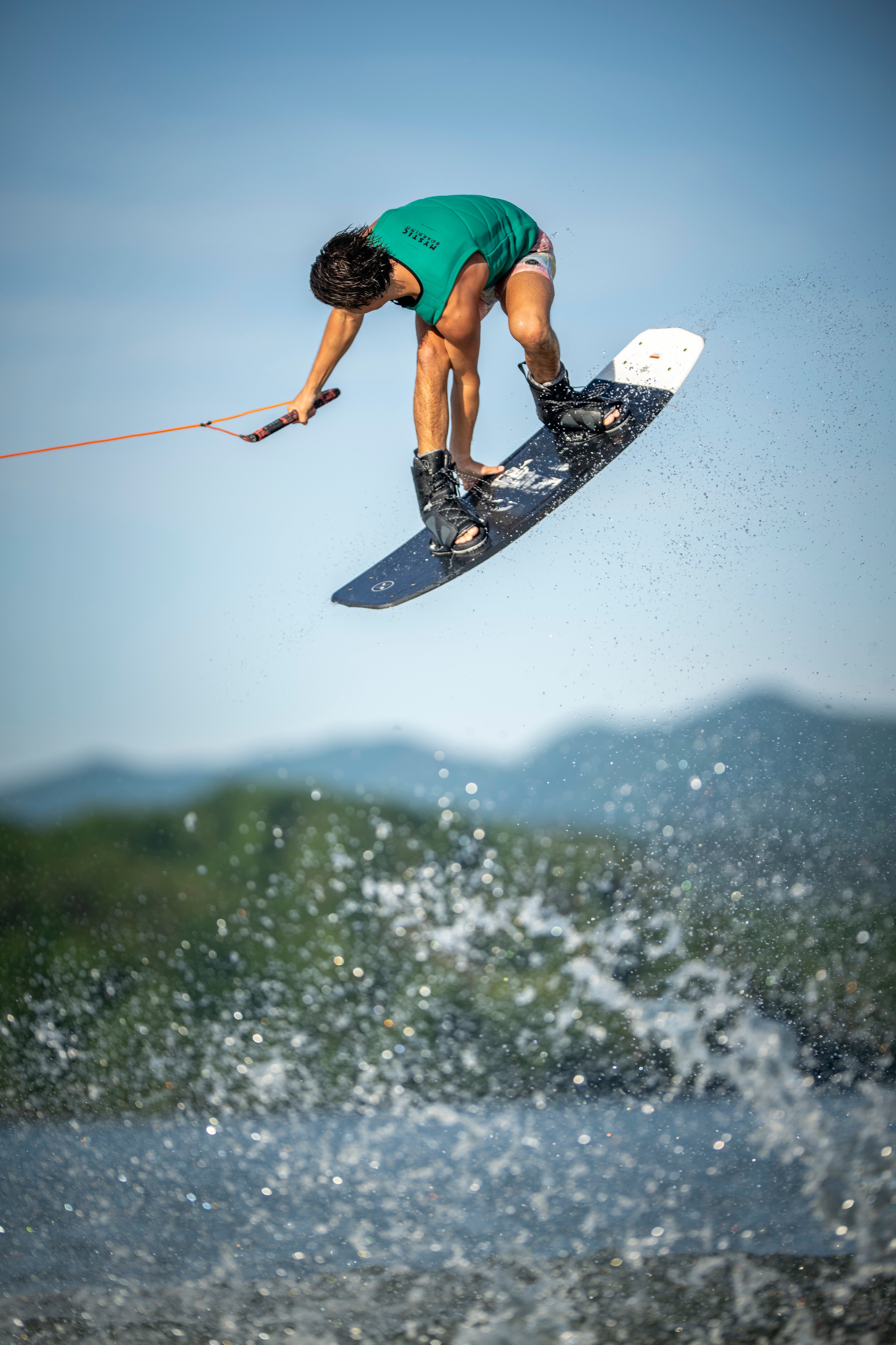 Person wakeboarding, airborne, with a blue sky and splashing water backdrop.