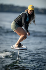 Rider on a Majik Karpet foil board, e-foiling with a life vest and yellow cap.