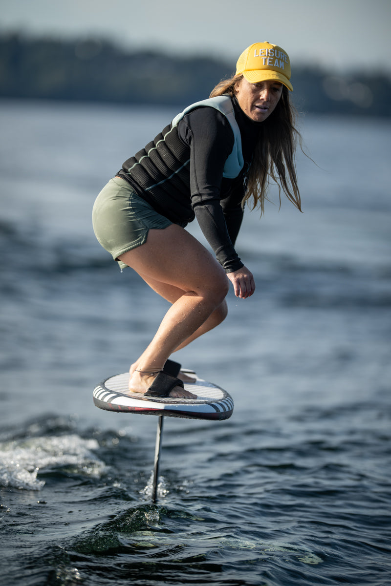 Rider on a Majik Karpet foil board, e-foiling with a life vest and yellow cap.