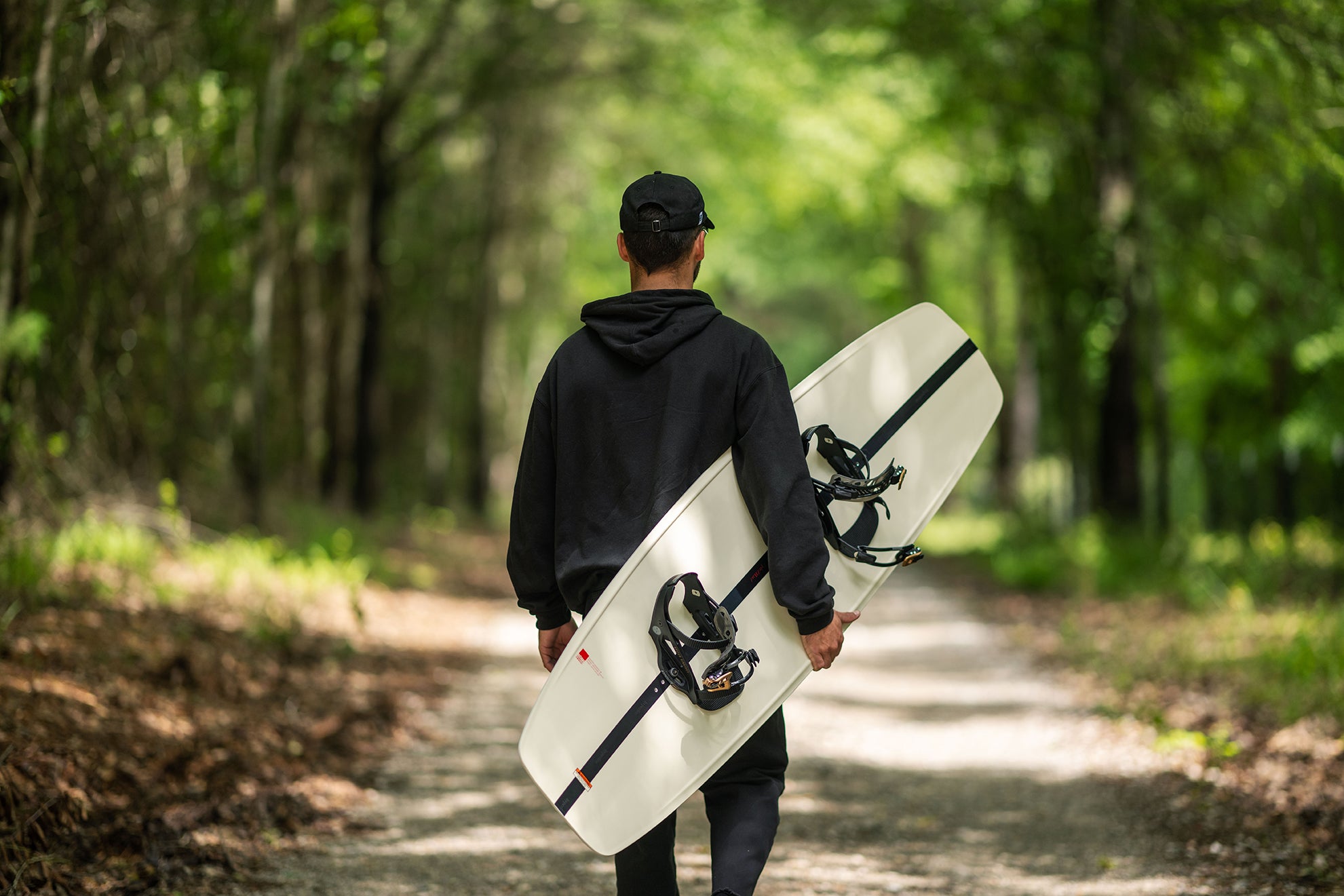 Person walking in a forest, holding a surfboard under their arm.