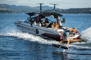 Person wake surfing on a Starship 3.4 behind a boat on a lake under a clear sky.