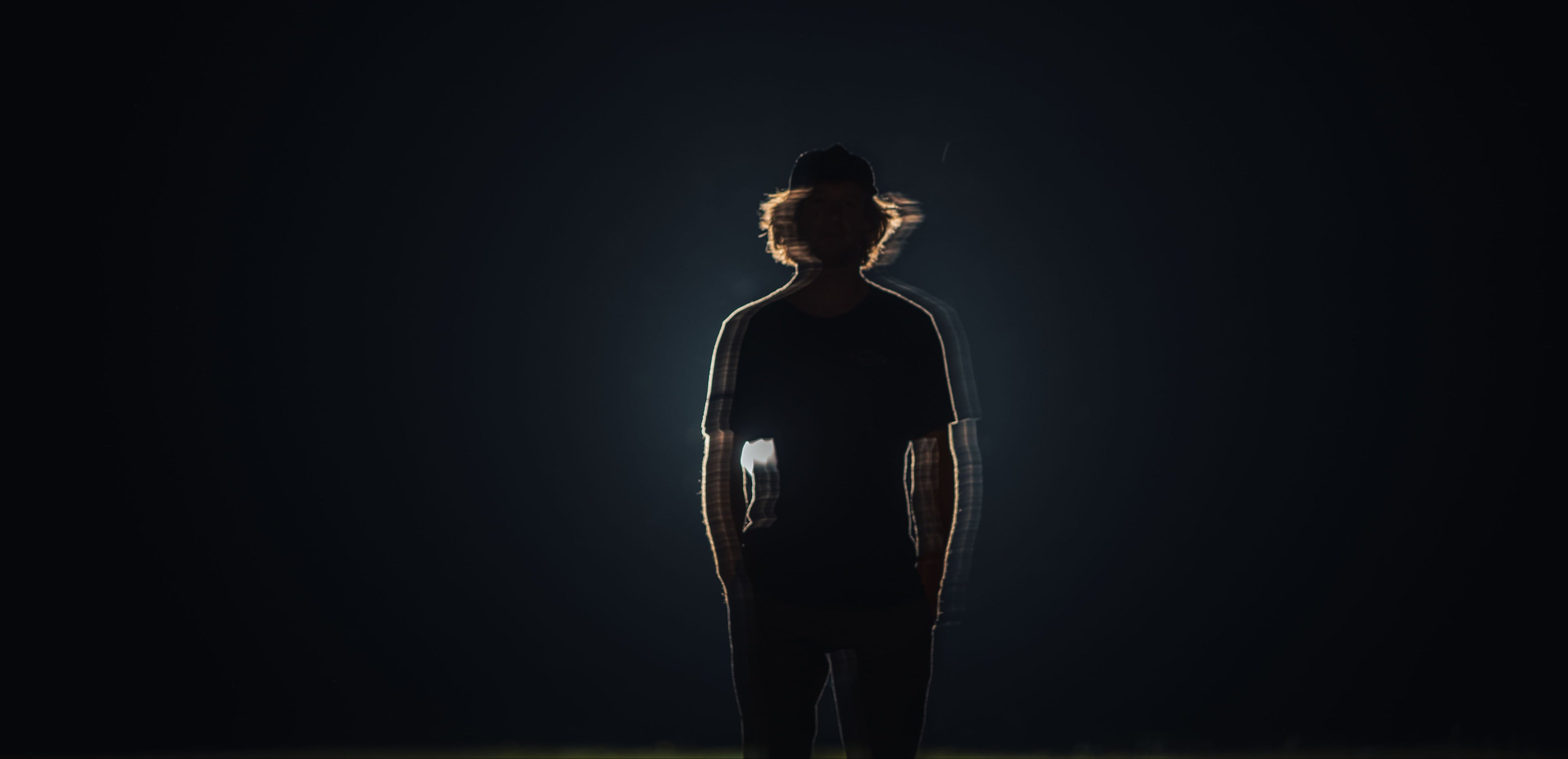 Silhouette of a person in a hat against a bright light and dark background.