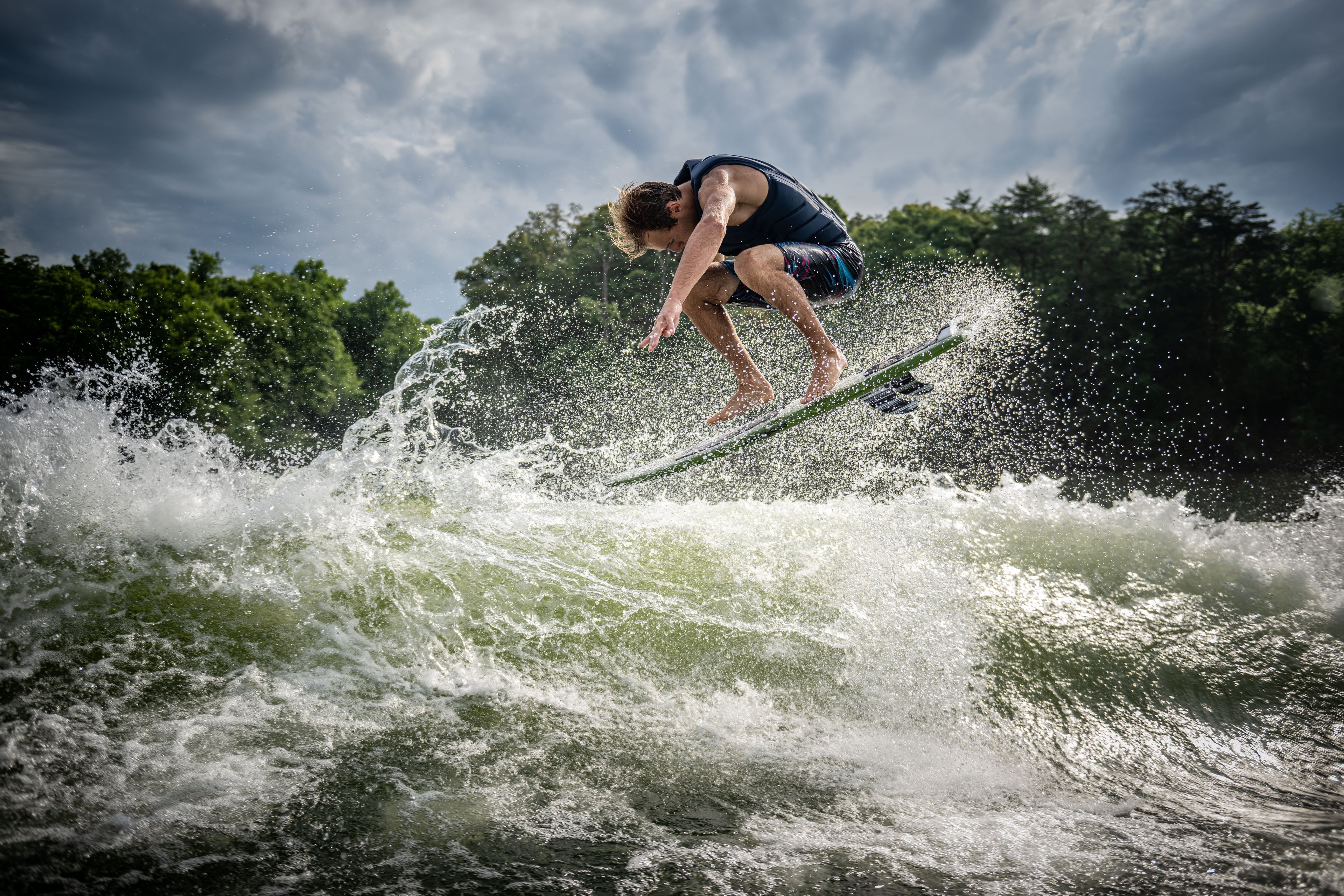 Person surfing on a wave, performing a jump under a cloudy sky.