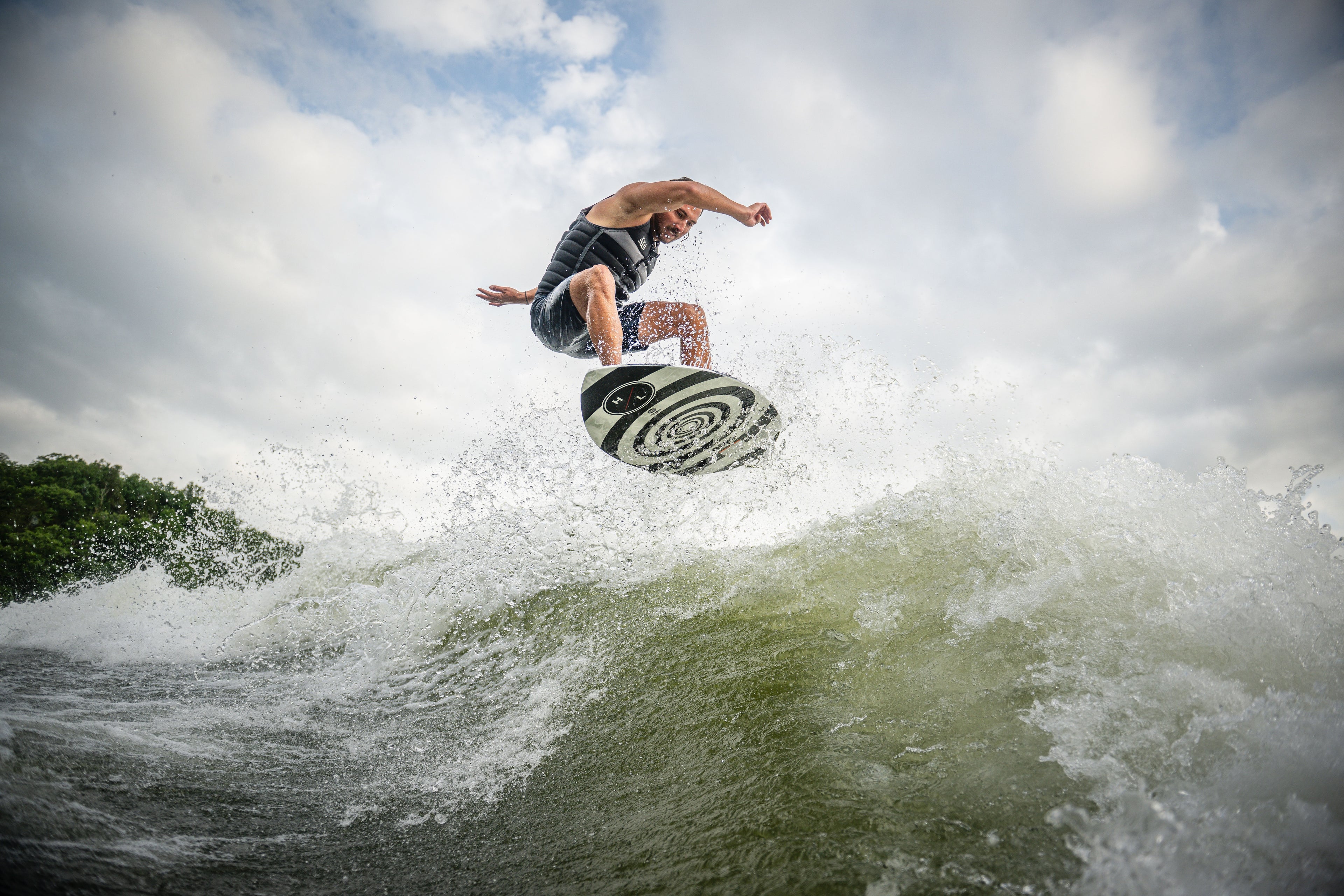 Person surfing on a wave, performing an airborne trick under a cloudy sky.