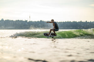 Person surfing with the Starship w/Falcon Foil Kit near a forested shoreline.