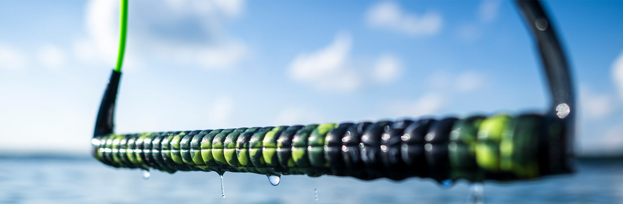 Close-up of a wet braided rope over water with a blue sky background.