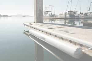 White inflatable dock bumper attached to a dock edge above calm marina water.
