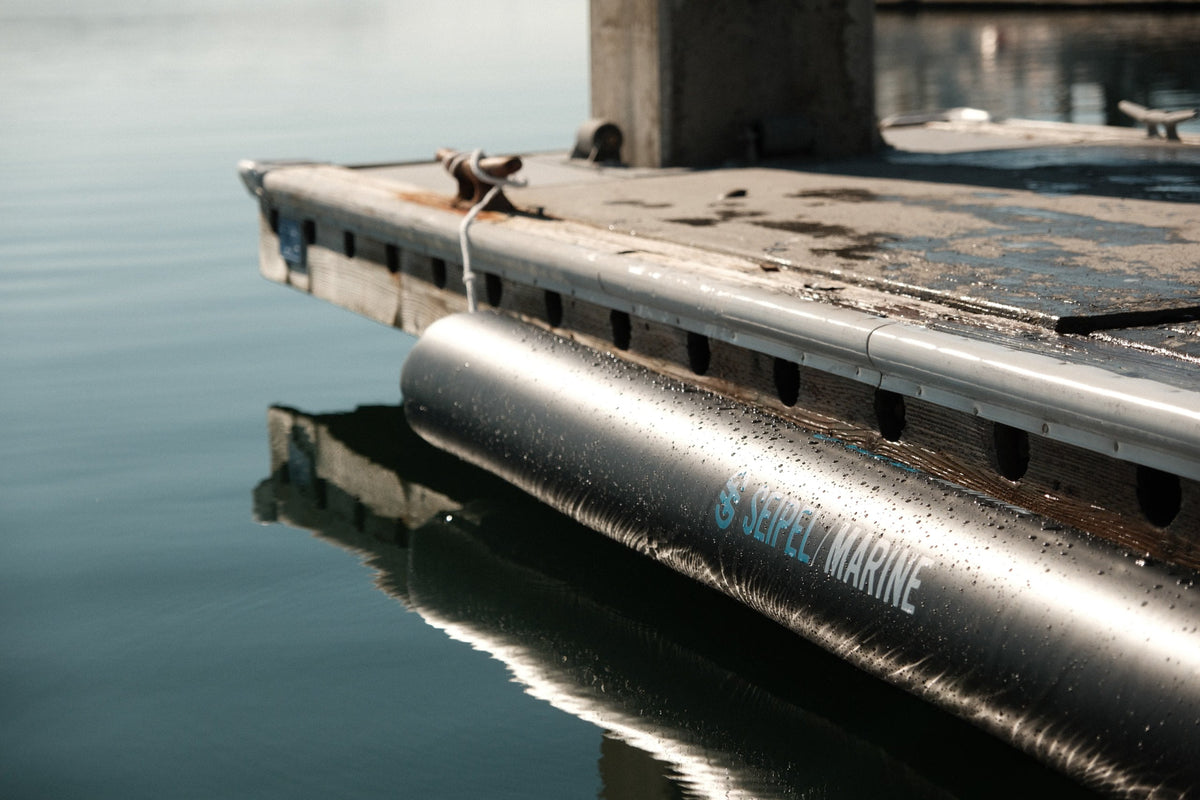 Close-up of a Seipel Marine inflatable dock bumper tied to a wooden dock above calm water.