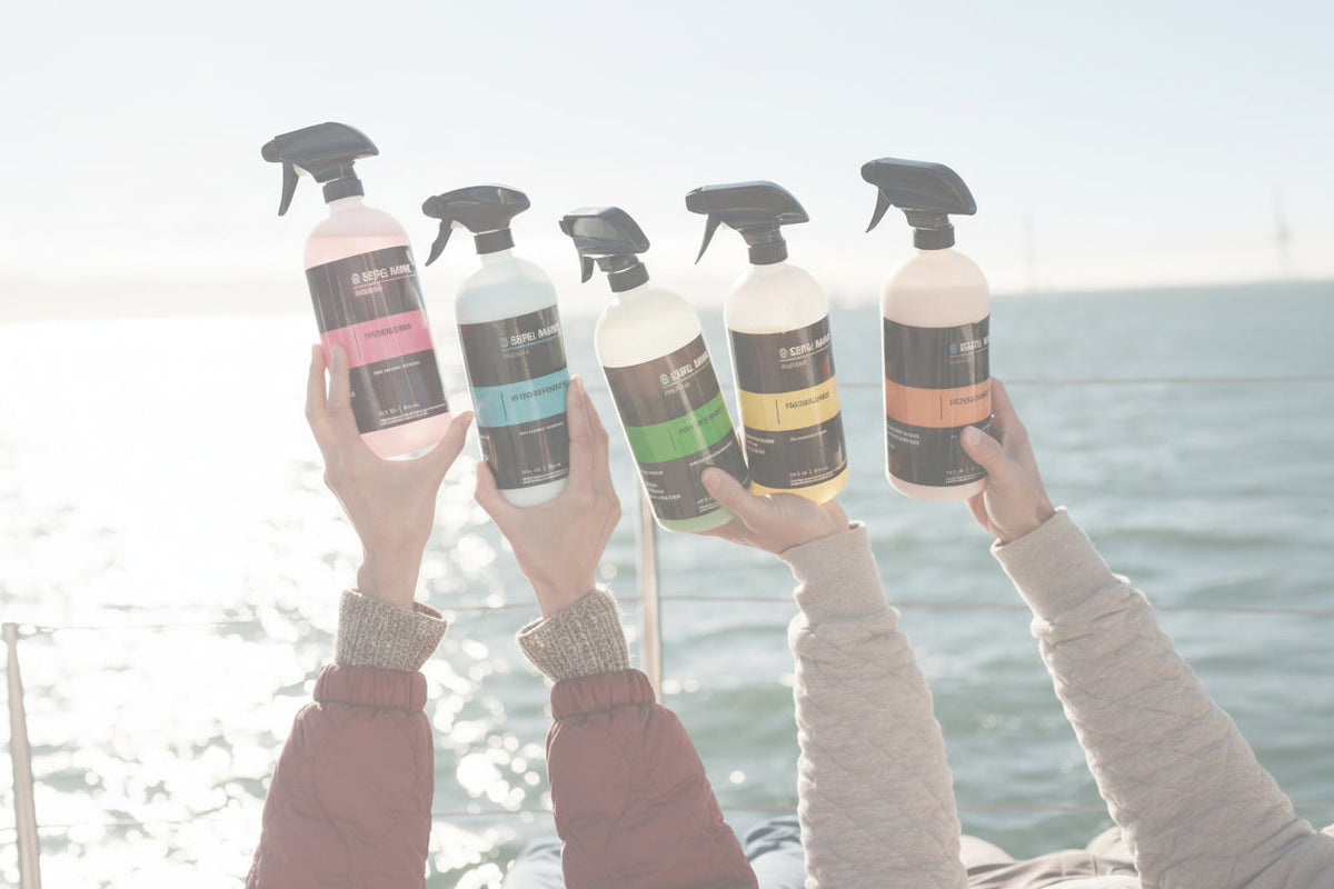 Hands holding five Seipel Marine premium cleaning spray bottles against open water in the background.