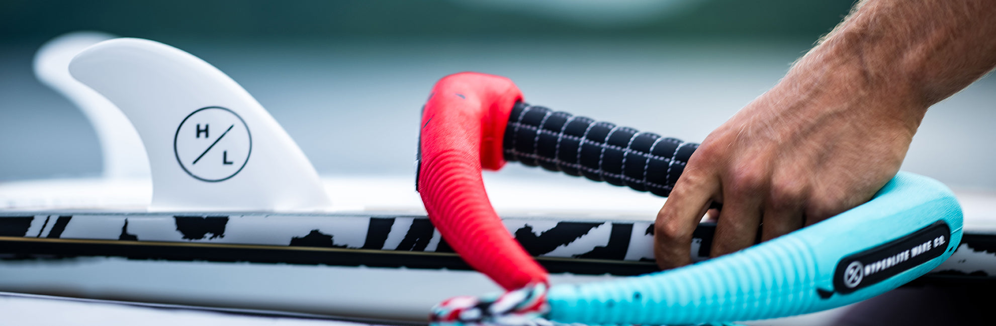 Close-up of a hand holding wakeboarding ropes near a board with a visible fin.