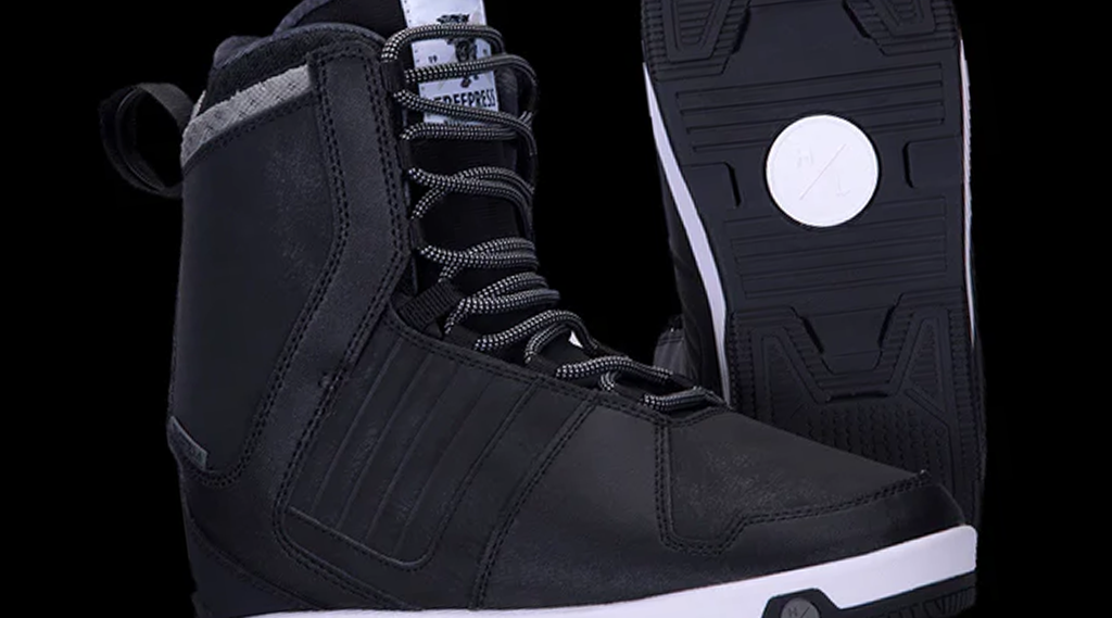 Black snowboarding boots with gray accents and white soles, isolated on a black background.