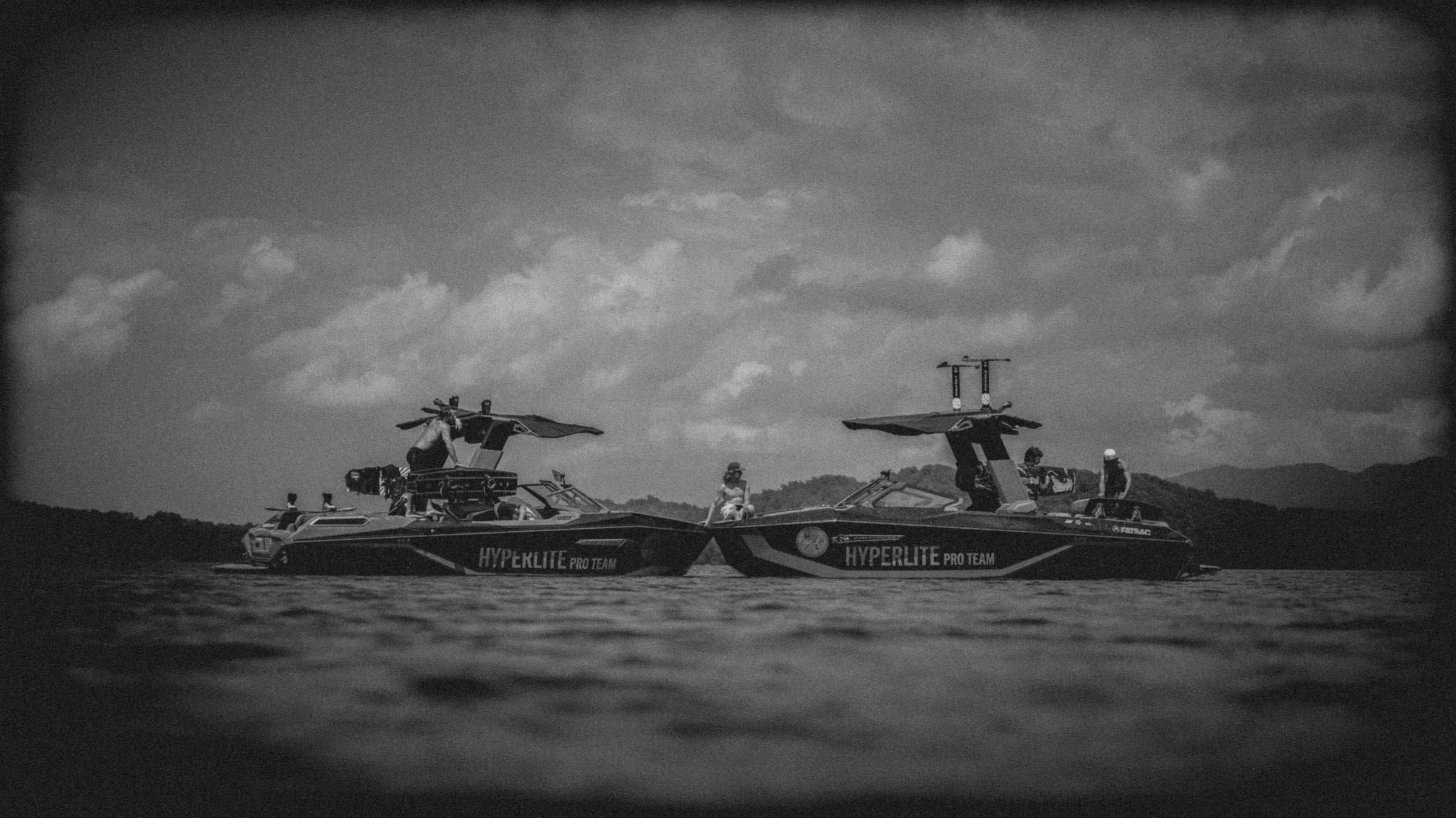 Black and white photo of two boats on water with 'Hyperlite Pro Team' branding against a cloudy sky with 4 people on board.