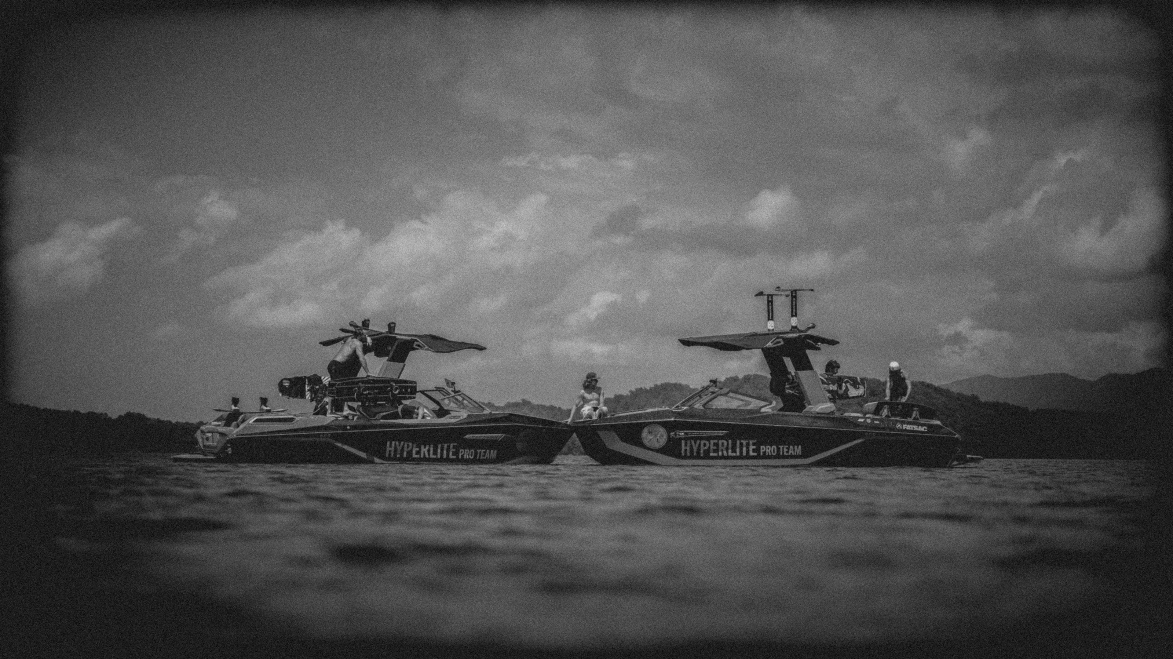 Black and white photo of two boats on water with 'Hyperlite Pro Team' branding against a cloudy sky with 4 people on board.