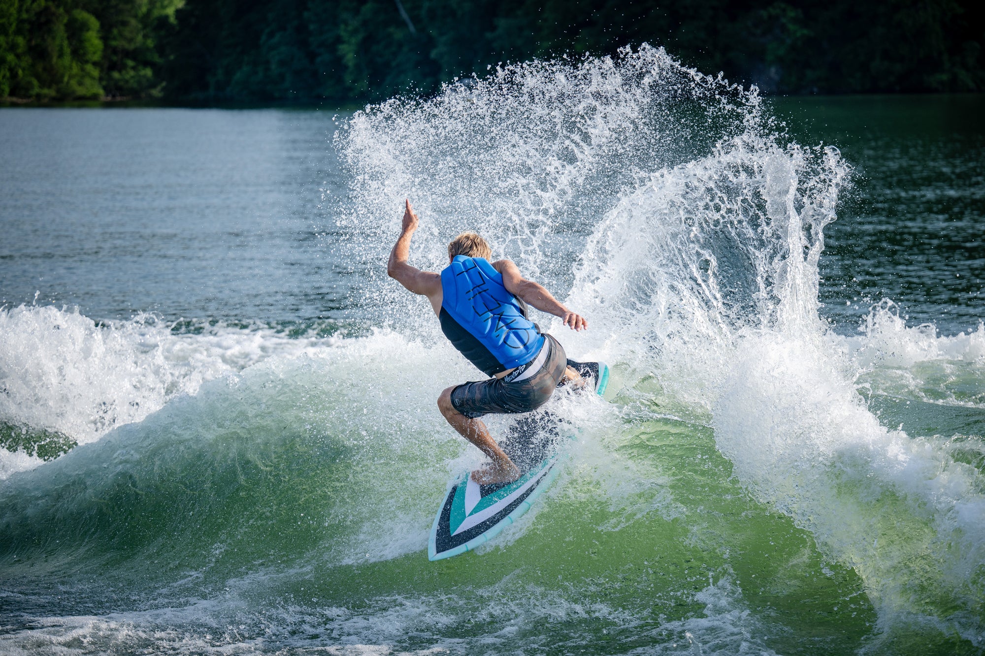 Person wakesurfing on a wave with a blue vest and black shorts.