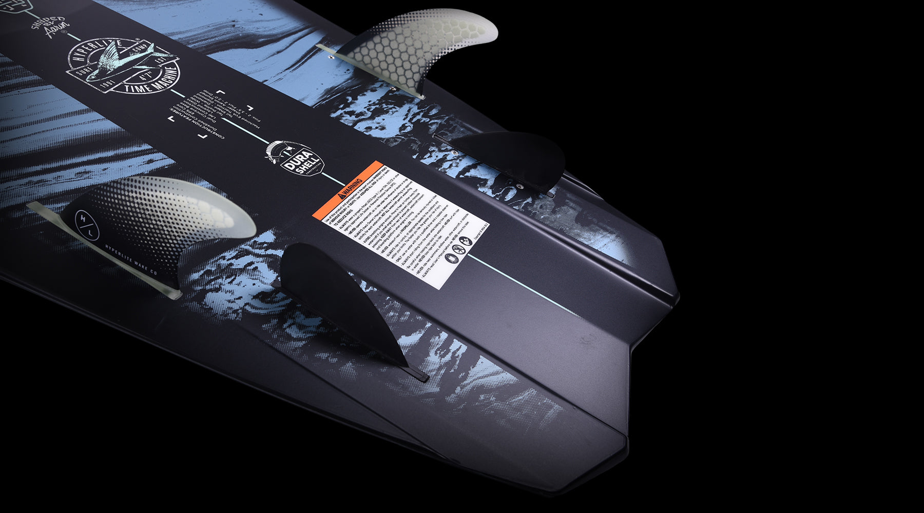 Close-up of a surfboards tail, showing fins and design details on a black background.